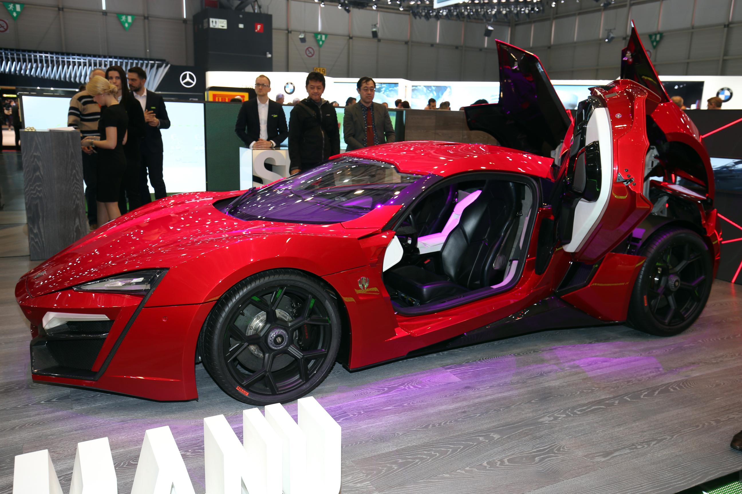A red Lykan Hypersport, facing left with scissor door open to reveal black and white leather interior.